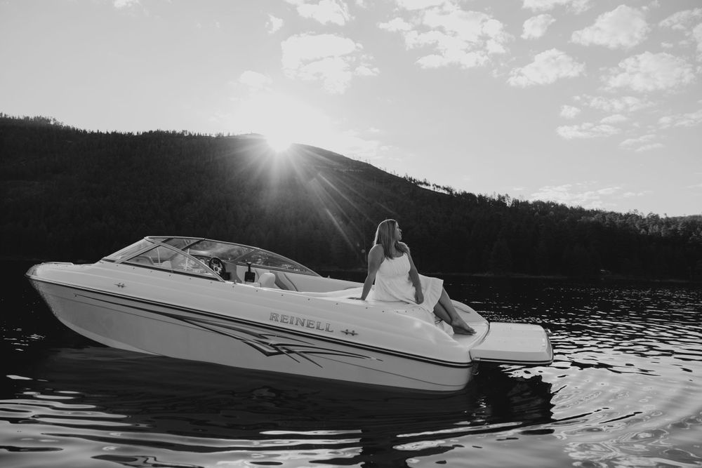 Black and white photo of woman on Reinell motorboat with sun rays over a mountain lake.
