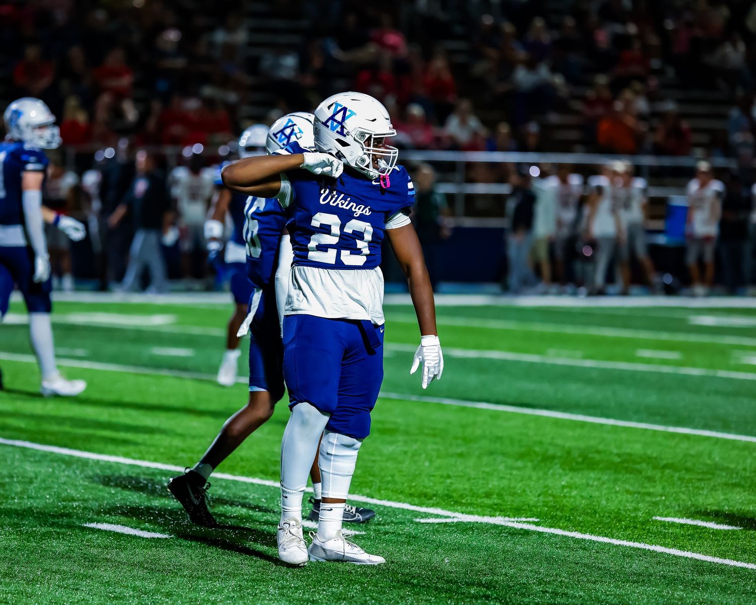 Football player in white and blue uniform number 23 celebrates on field during nighttime game.