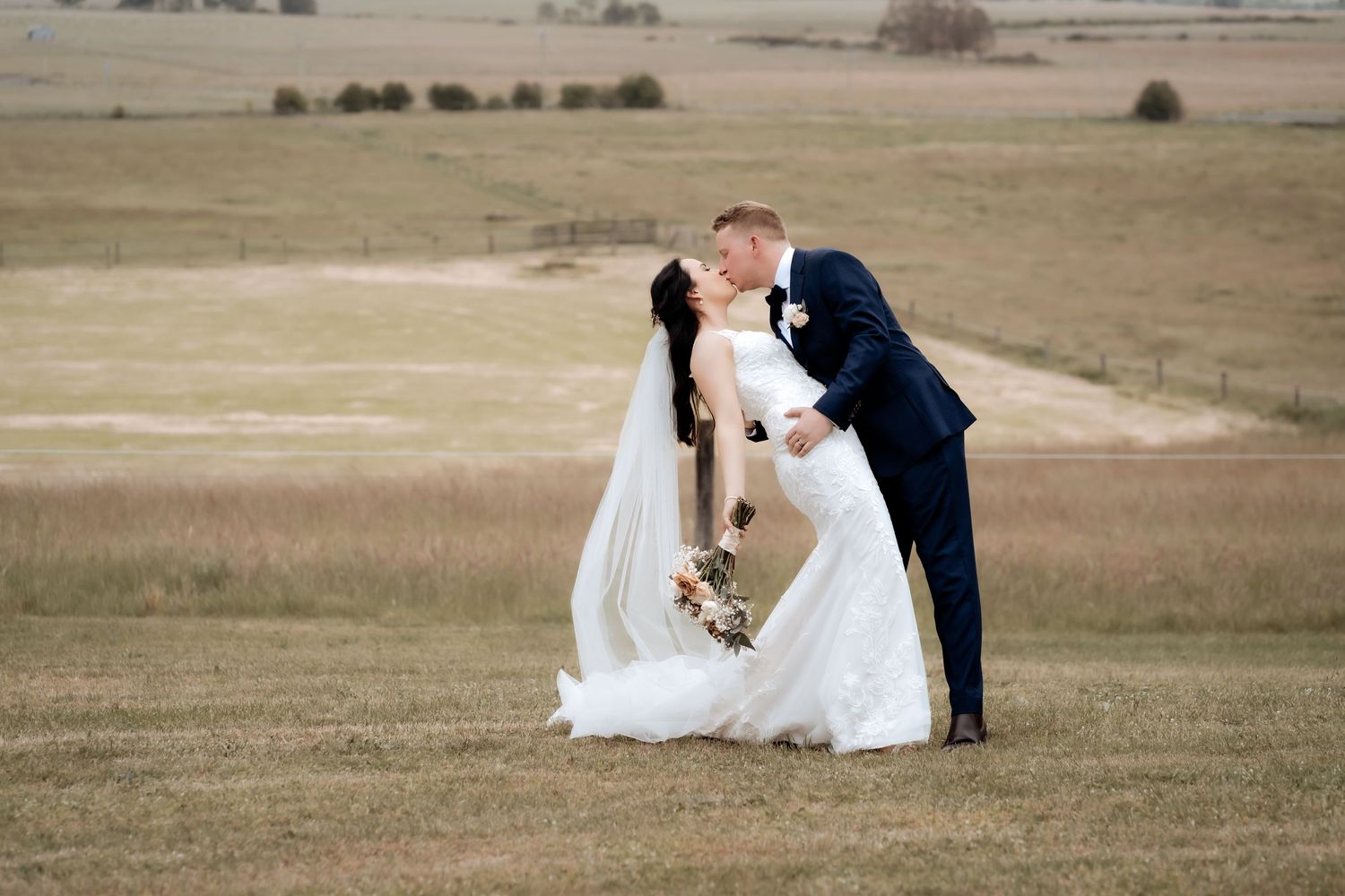 Romantic wedding portrait of couple in formal attire embracing in an open field.