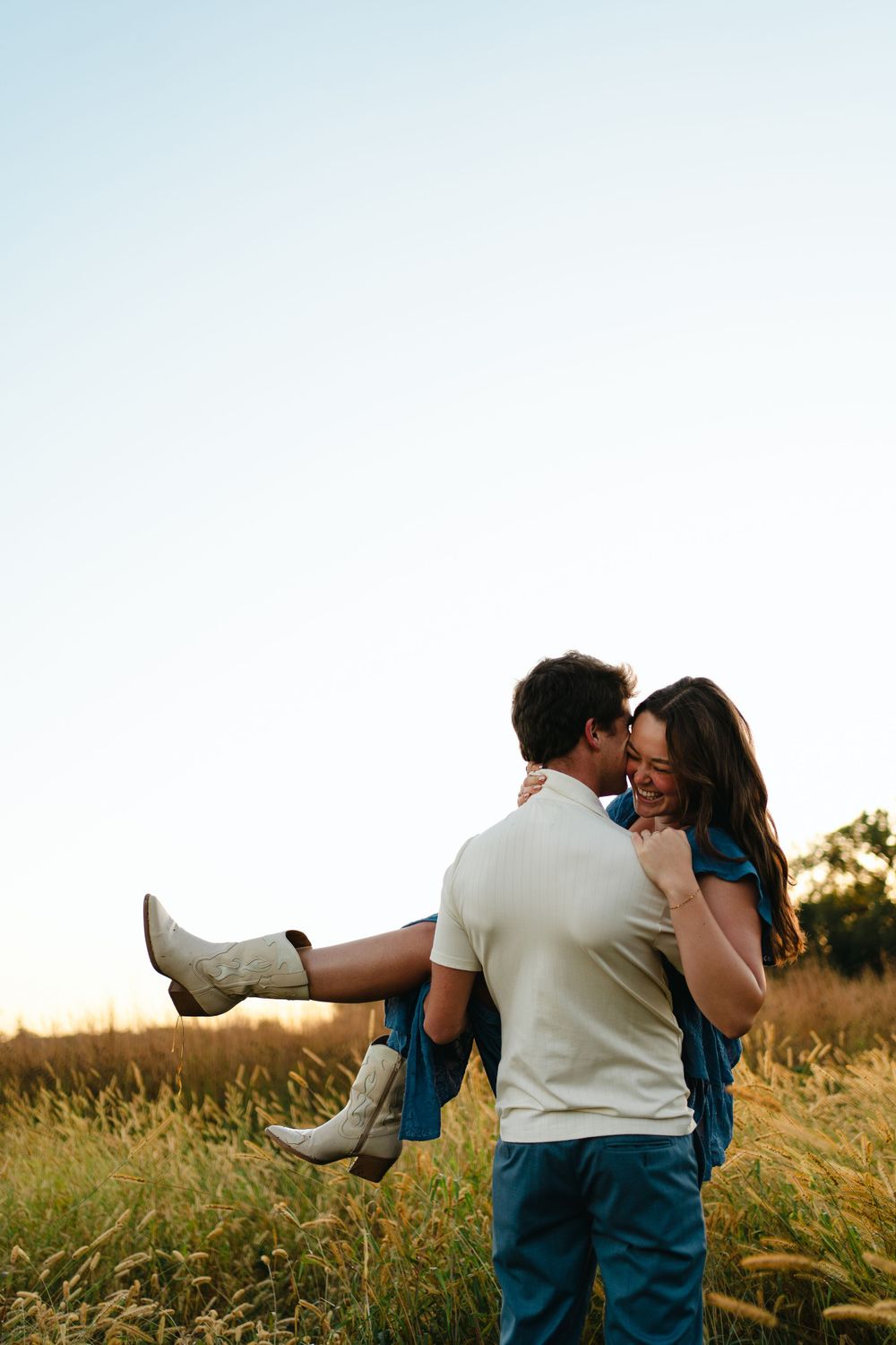 A couple shares a playful moment in a sunlit field, with white boots prominently featured.