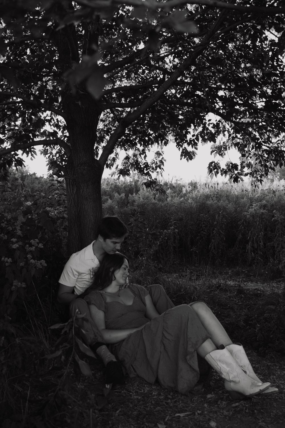 A tender black and white moment shared under a large tree at dusk.