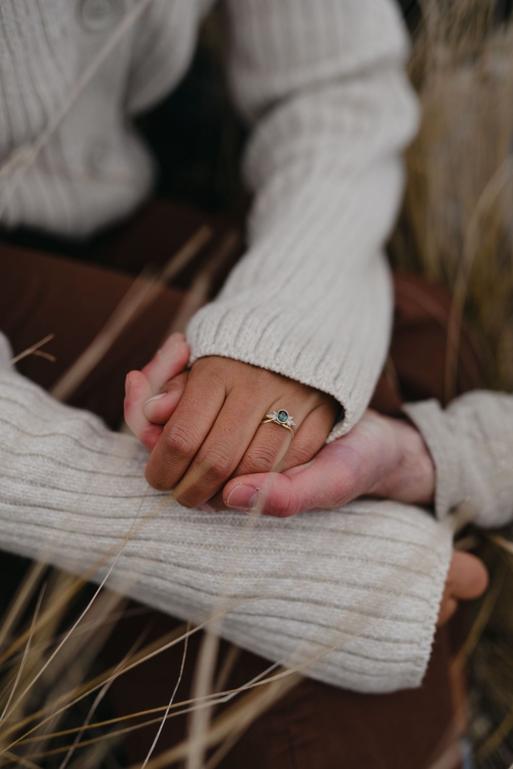 Close-up of clasped hands in white knit sweaters with an engagement ring.