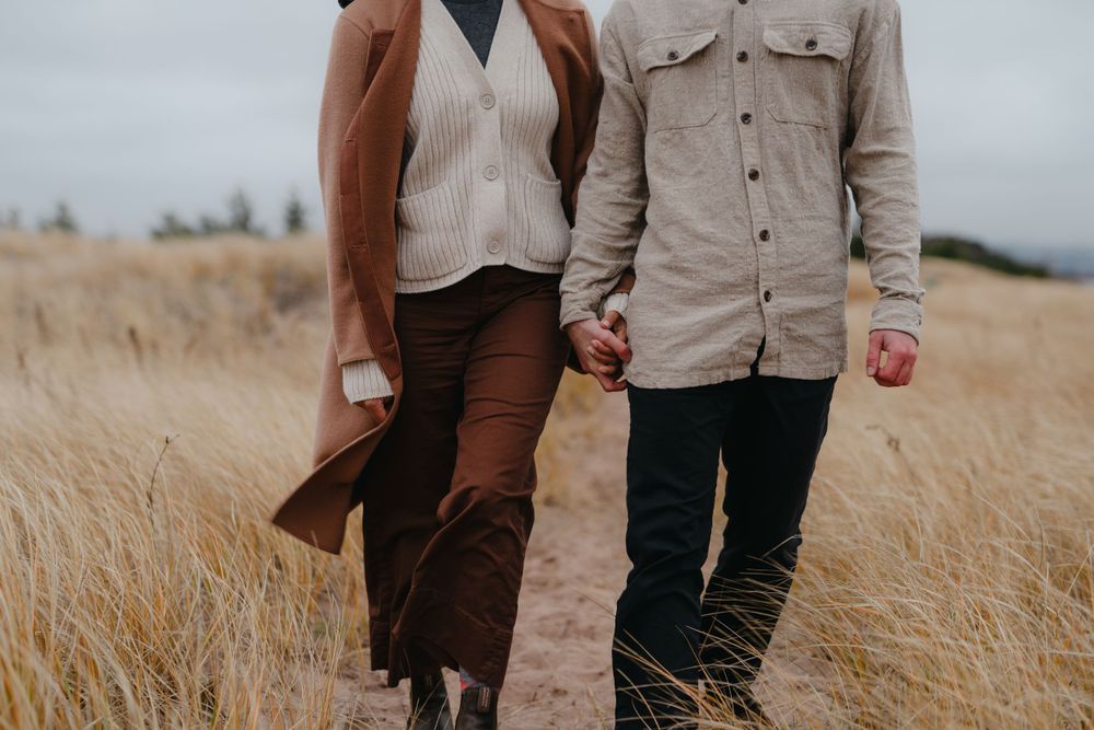 A couple walking together through tall grass in autumn clothing.