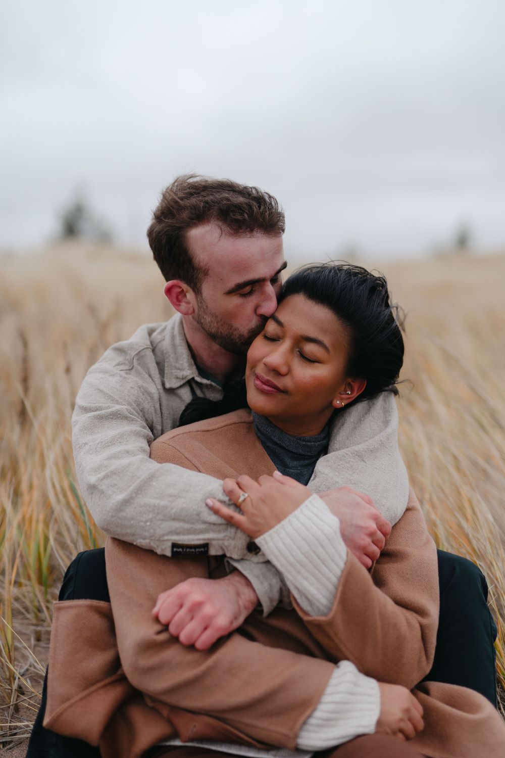 A tender embrace between a couple sitting in a golden wheat field.