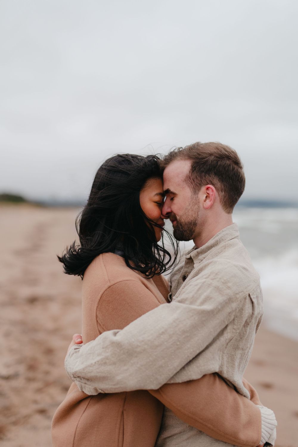 An intimate moment between a couple embracing on a cloudy beach.