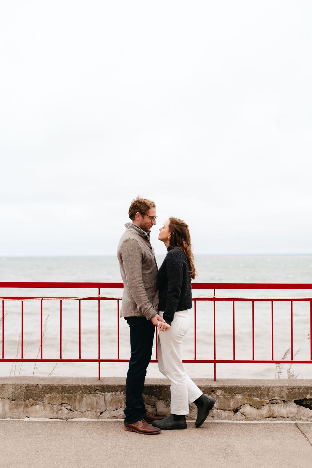 A couple shares an intimate moment against a red railing overlooking a misty ocean view.