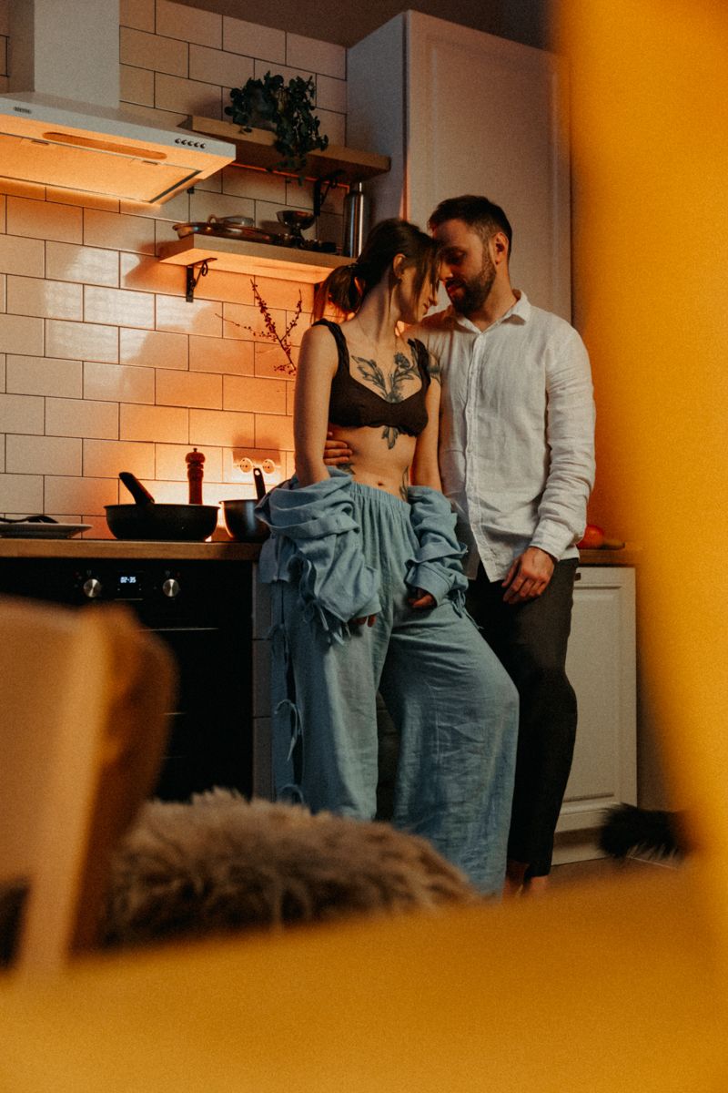 Couple sharing intimate moment in modern kitchen with warm lighting and tile backsplash.