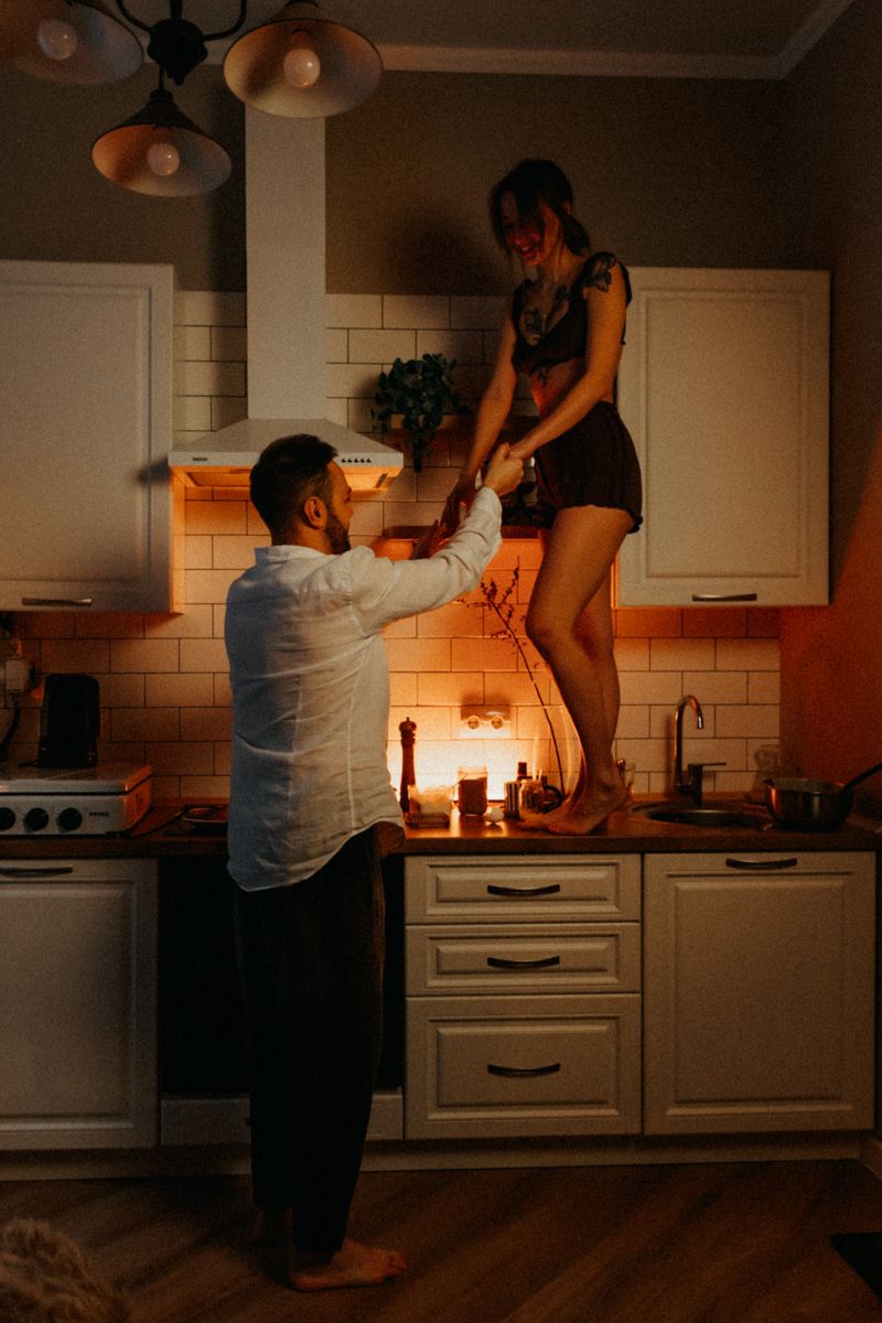 Romantic scene in kitchen as couple shares playful moment with candlelight.