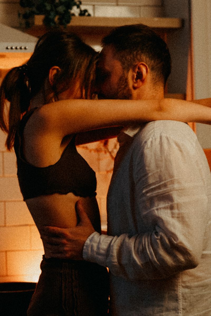 Couple embracing intimately in kitchen with warm ambient lighting.