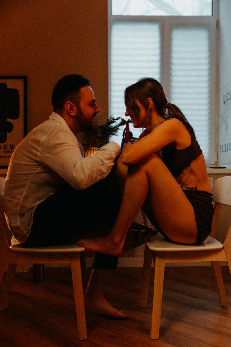 Couple sitting close together on wooden stools in intimate conversation.