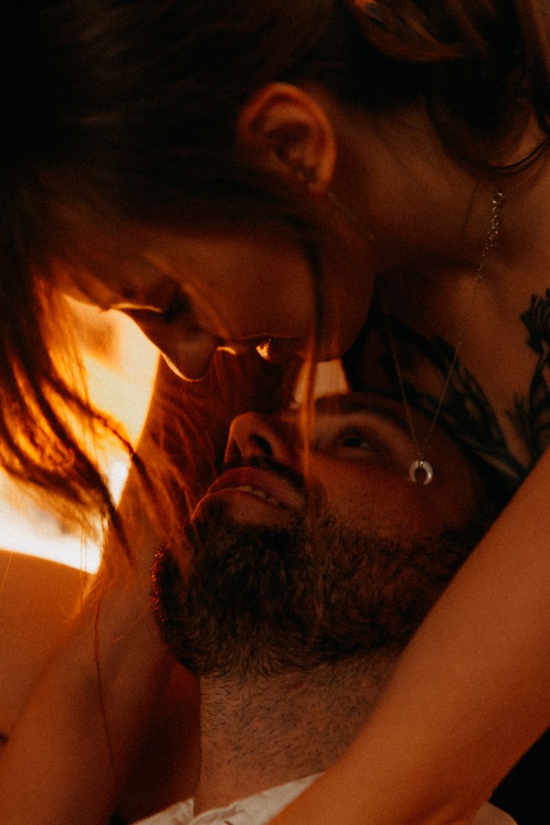 Close-up intimate photo of a couple in warm amber lighting sharing a romantic moment.