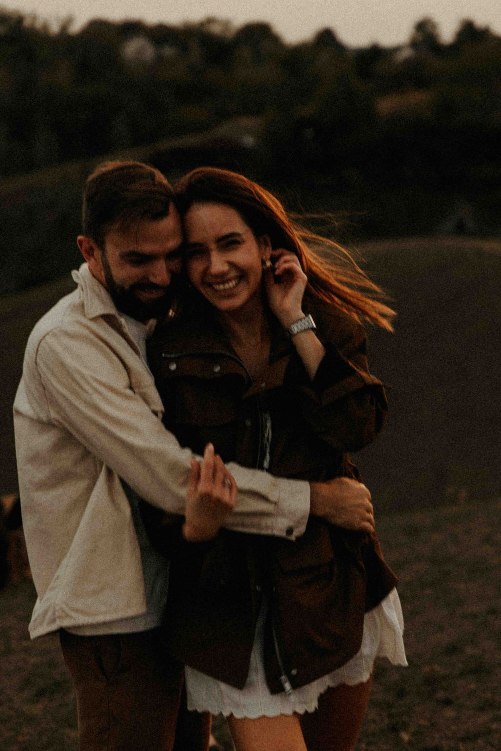 A joyful couple embraces outdoors at sunset, laughing together in a candid romantic moment.
