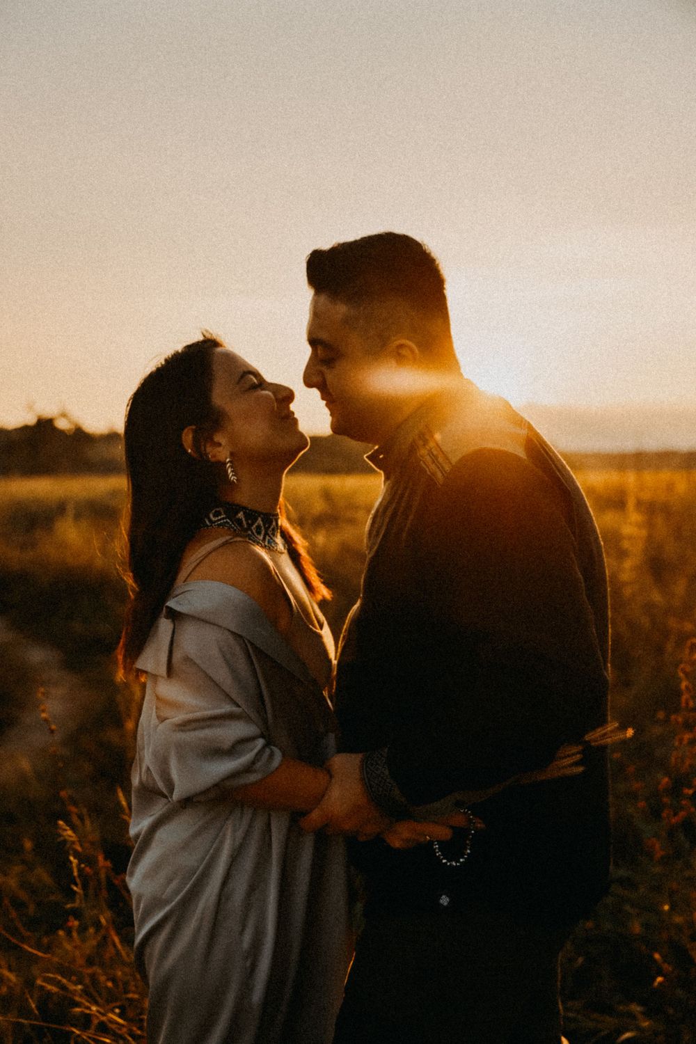 Romantic silhouetted couple embrace in golden sunset light while standing in a serene field of grass.