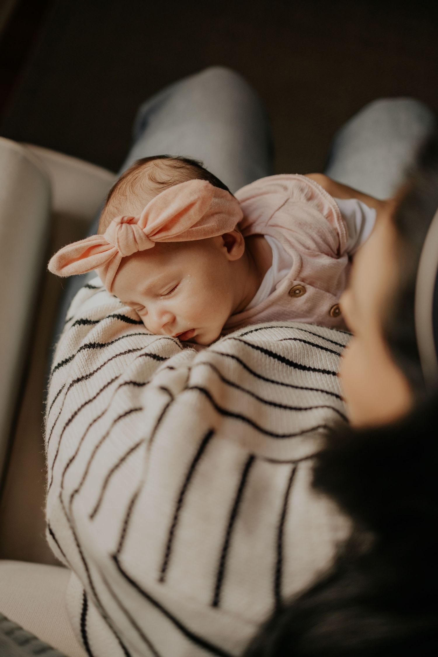 Sleeping newborn wrapped in striped blanket wearing peach bow headband in soft natural lighting.