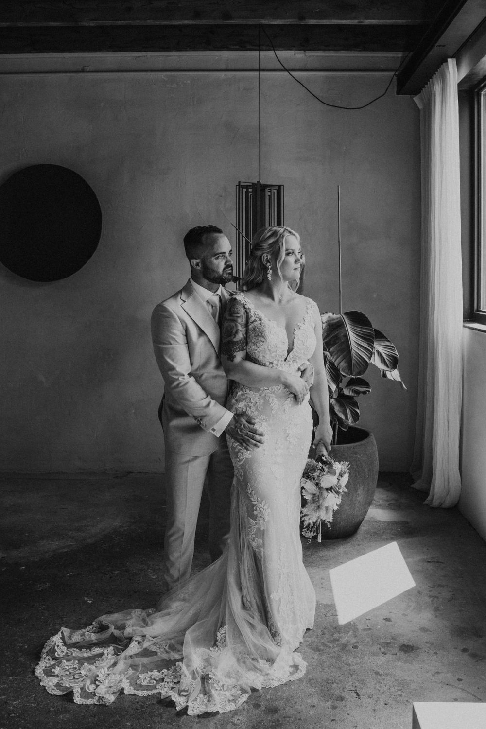 A romantic black and white wedding photo showing a couple in formal attire standing together in an industrial space.