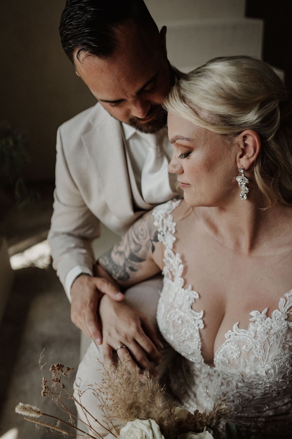 Intimate wedding portrait showing tender moment between couple in white attire with lace details and soft lighting.