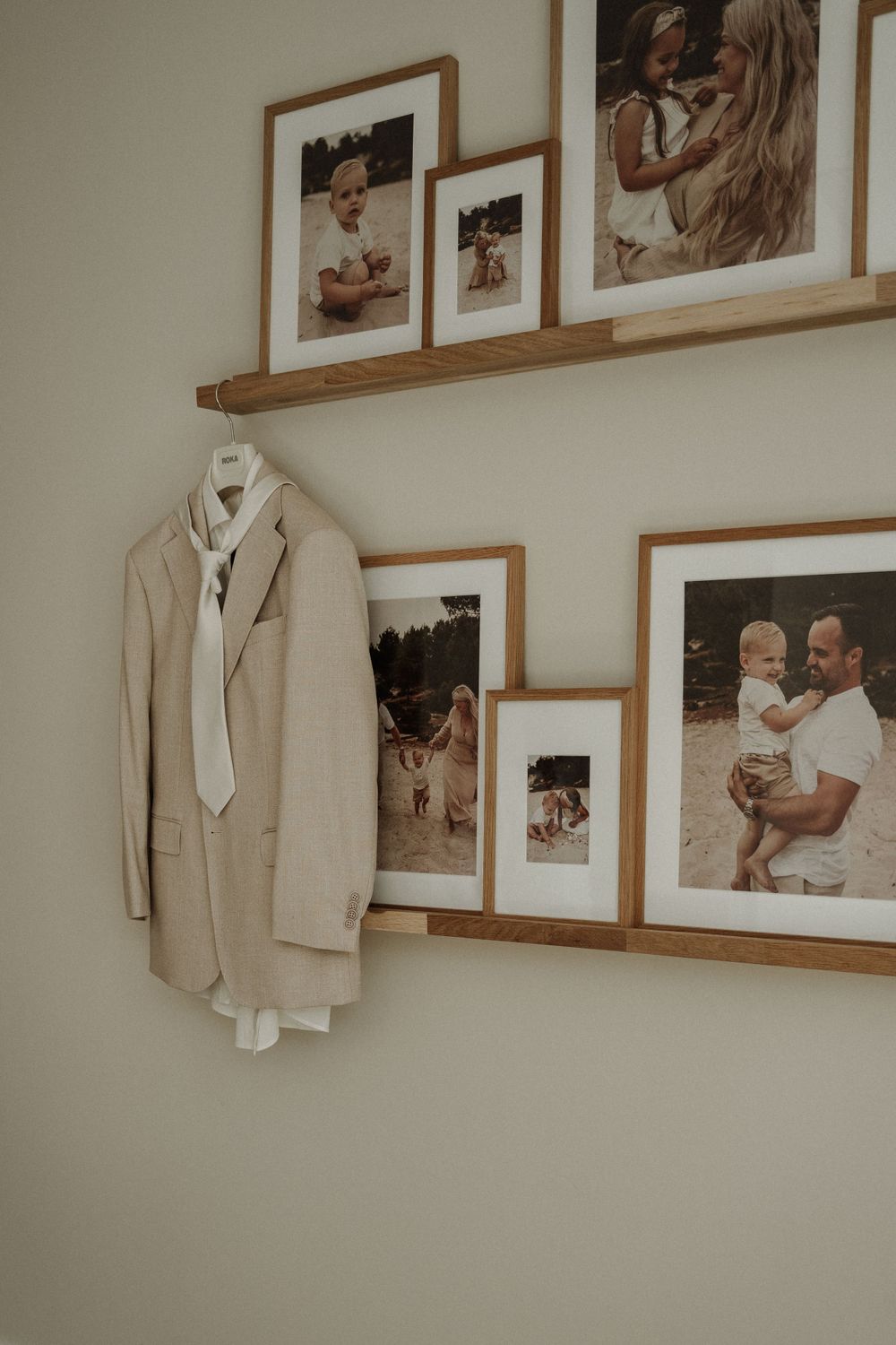 A beige suit jacket hangs on a wall next to framed family photographs displayed on wooden shelves.