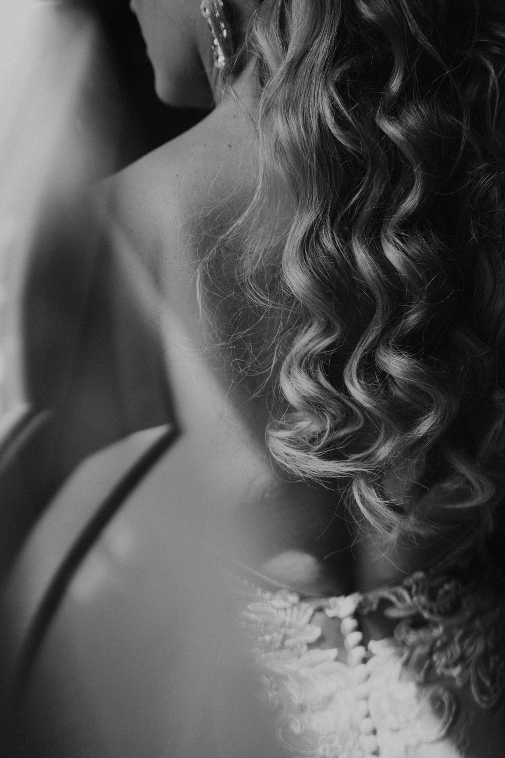 Black and white close-up of elegant curled hair cascading down a neck, with delicate lace detail visible.