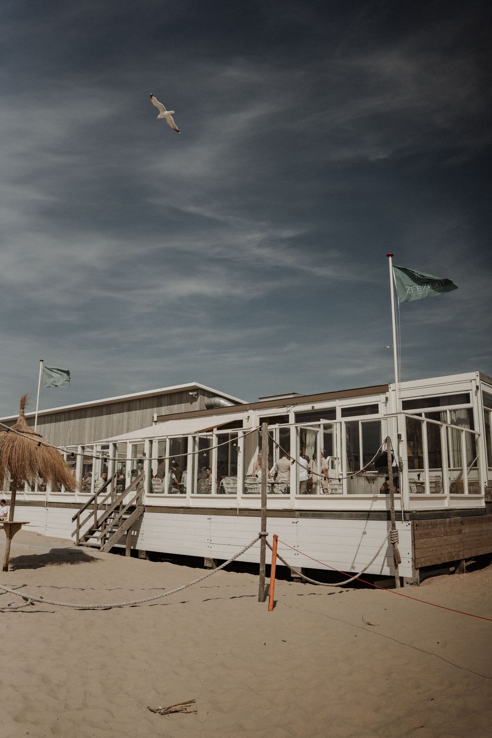 A beachfront wedding venue with white deck and flags under moody skies with a seagull flying overhead.