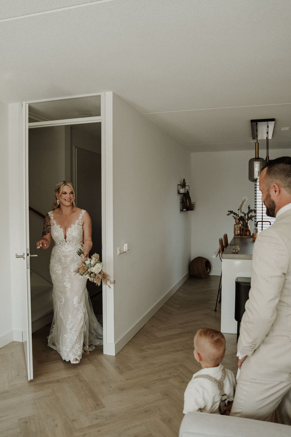 A heartwarming first look moment in a modern home with herringbone floors and white walls.