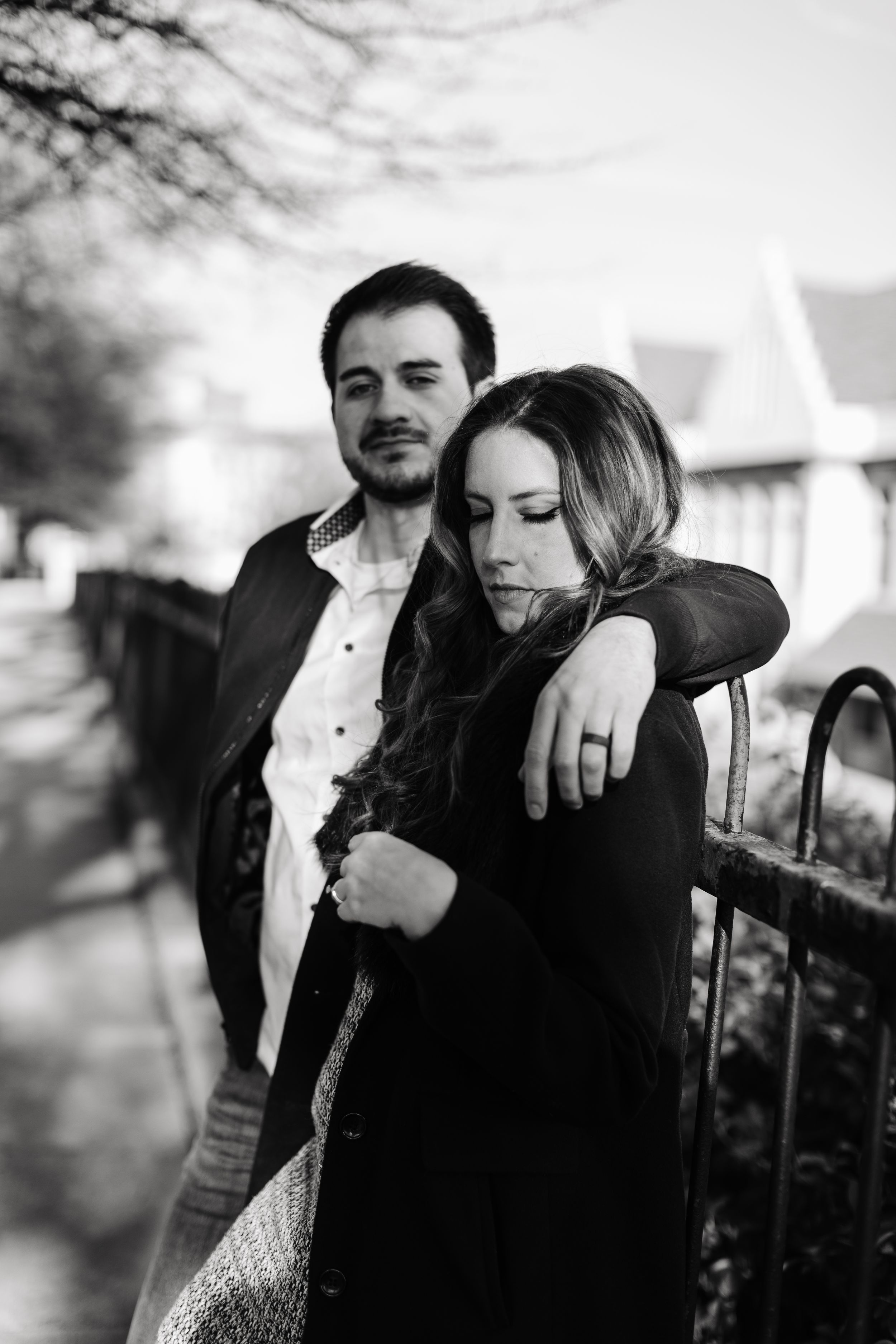 A black and white portrait of a couple embracing outdoors against an iron railing.