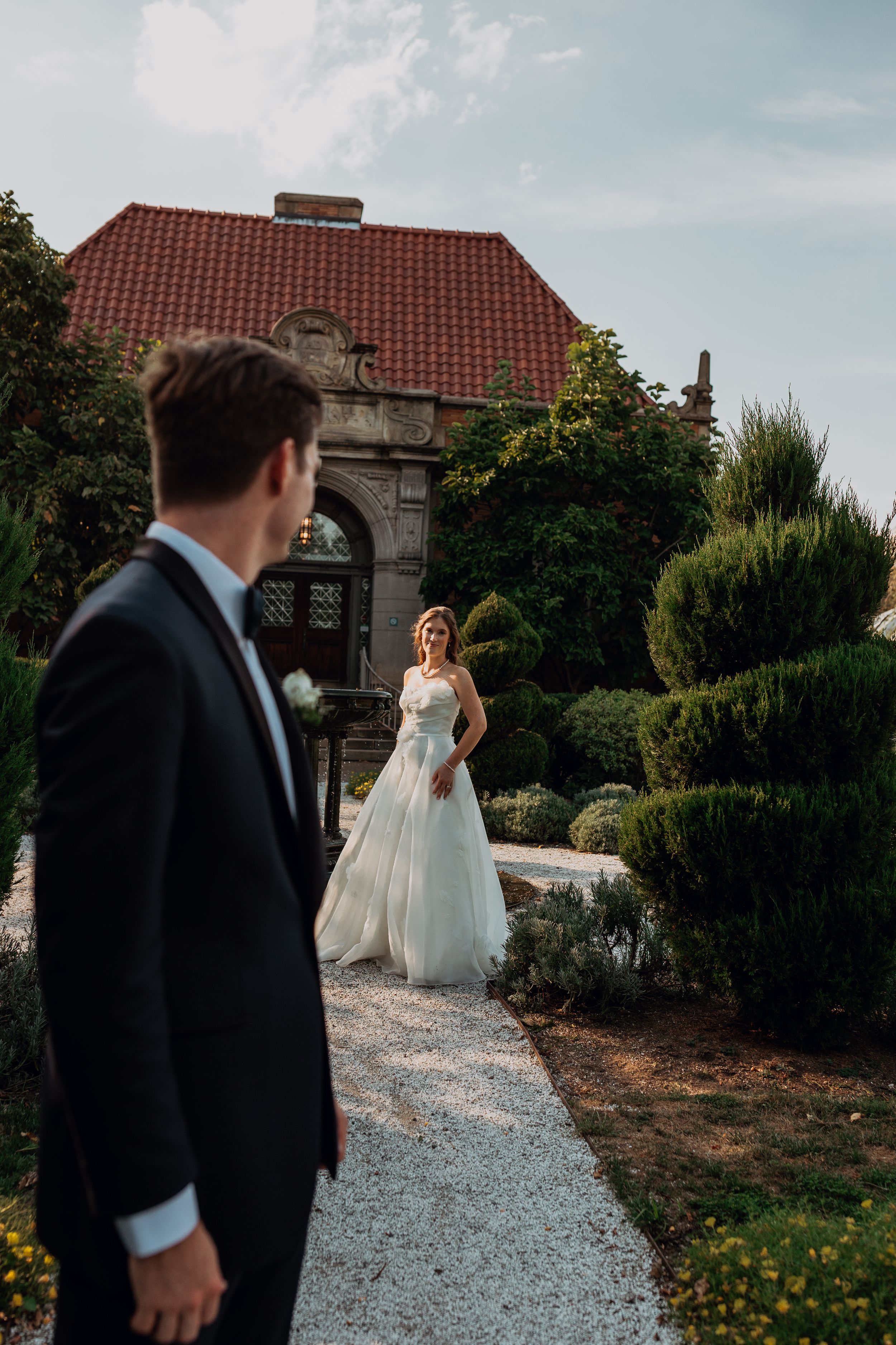 Wedding scene at historic building with stone archway and manicured garden path.