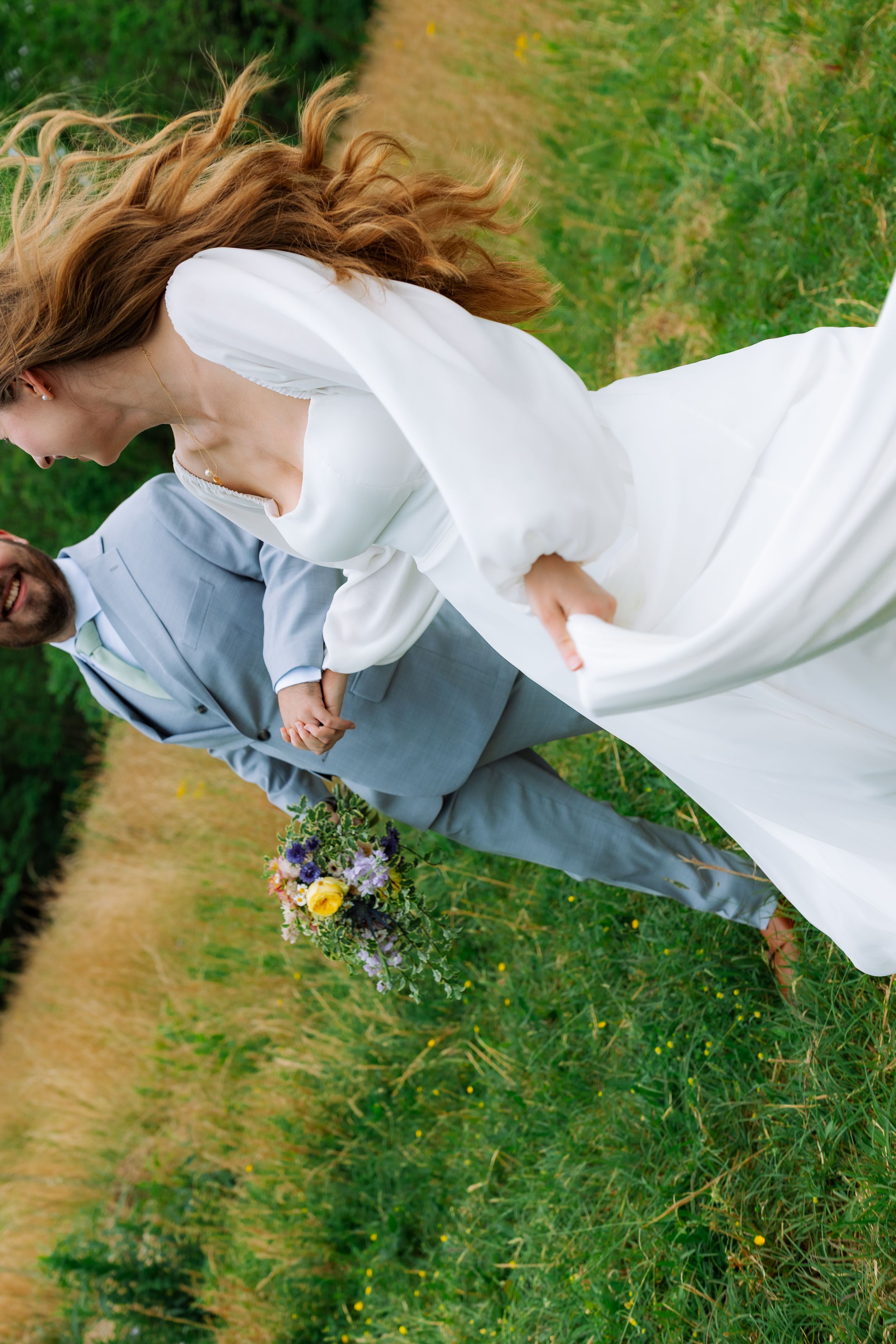 A couple dances in a grassy field with the bride's white dress flowing in the wind.