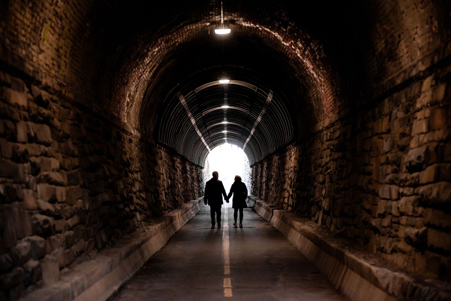 Two silhouettes walking through illuminated stone tunnel with dramatic lighting.