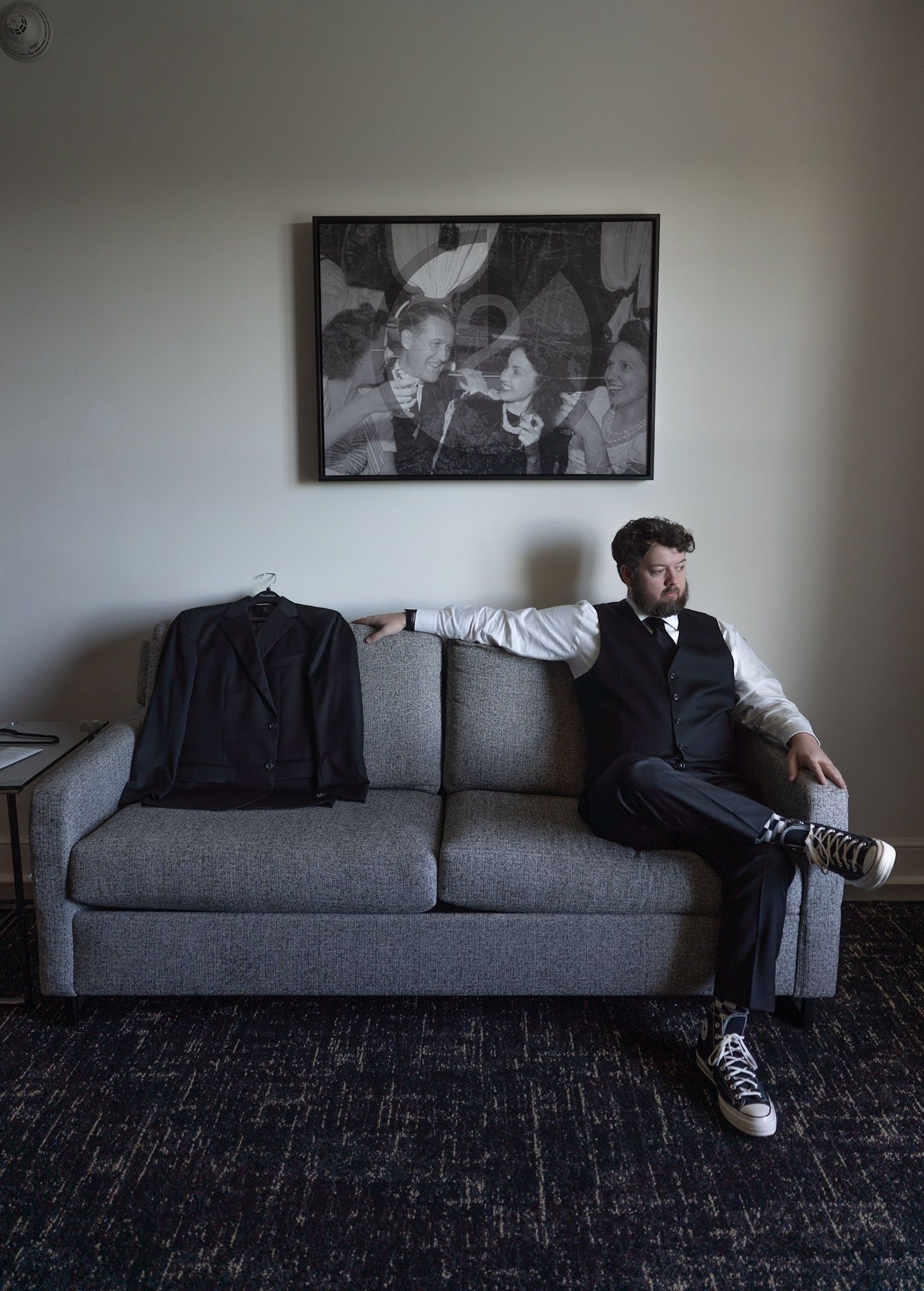 Artistic portrait of someone sitting on a grey couch with black and white artwork in background.