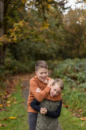 Two children in casual wear playing and laughing in an autumn forest setting.