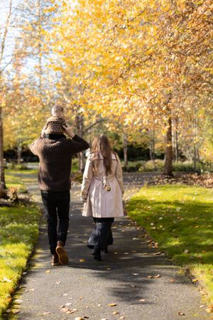 Two people walking down a sunlit path with golden autumn leaves overhead.
