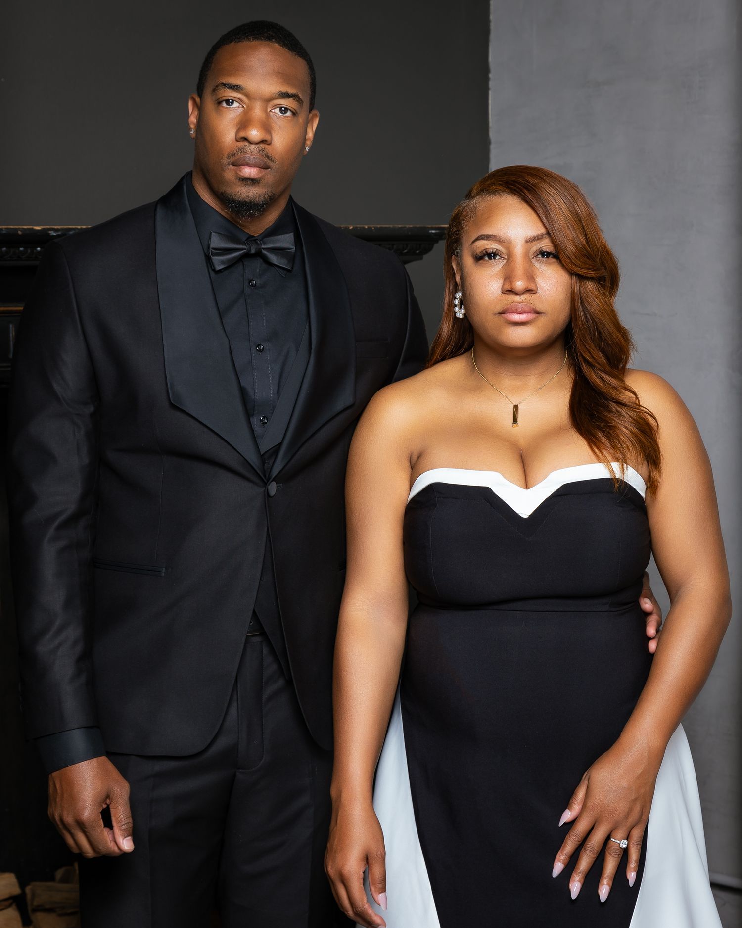Couple in formal attire posing for a stylish portrait against a dark background.
