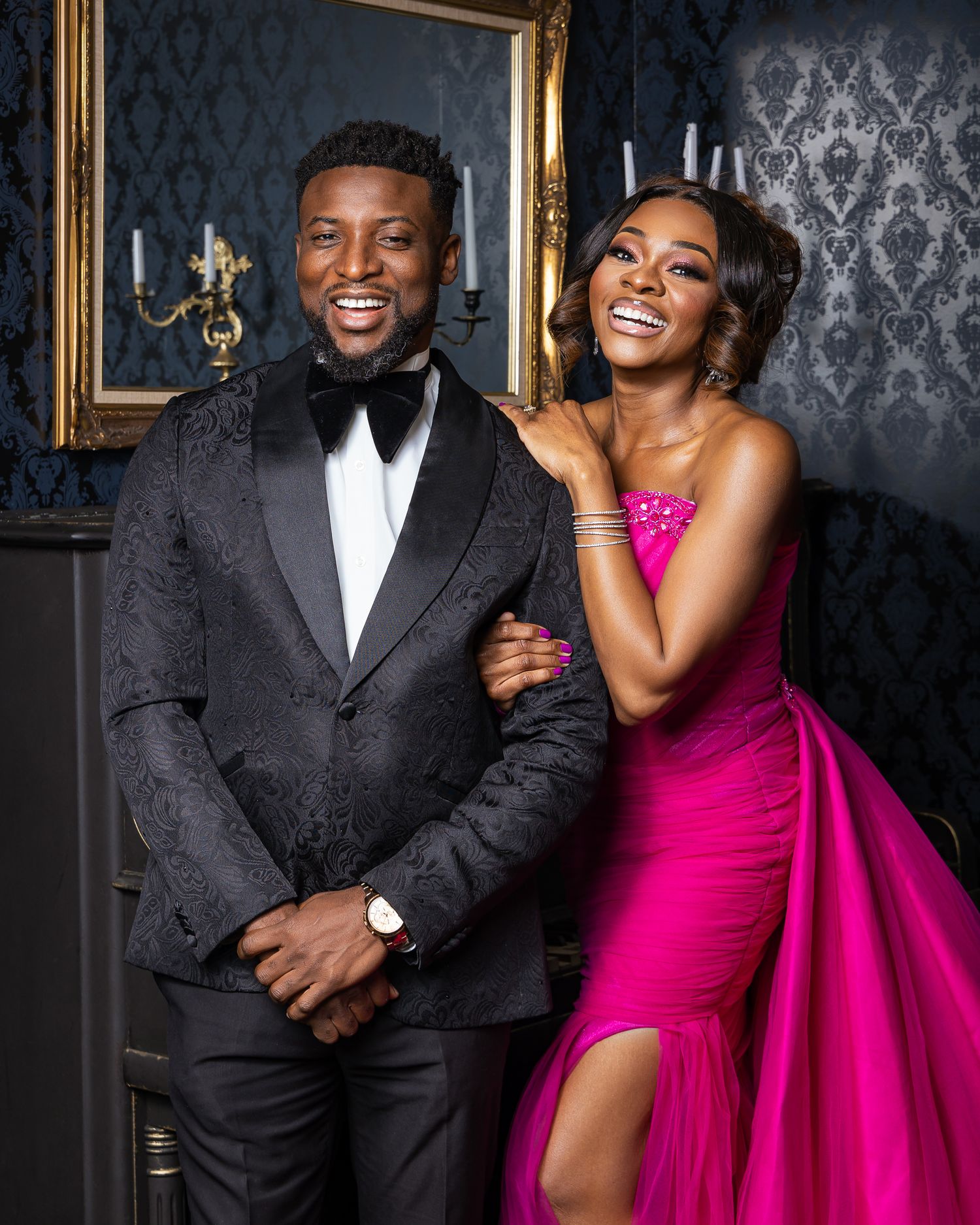 Elegant couple in formal wear posing against dark patterned background.