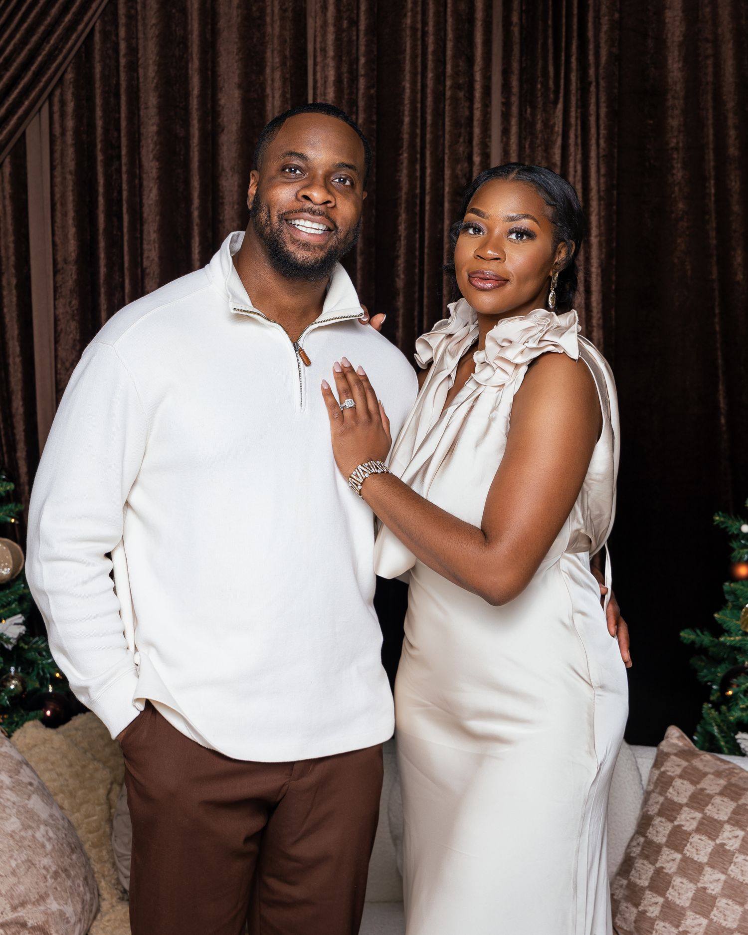 Couple in white outfits posing for a holiday portrait with Christmas decorations.