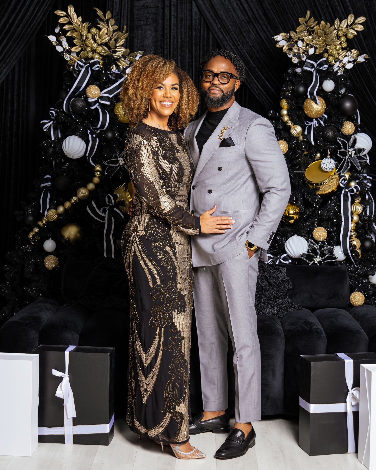 Couple in formal wear posing with gold and black Christmas decorations.