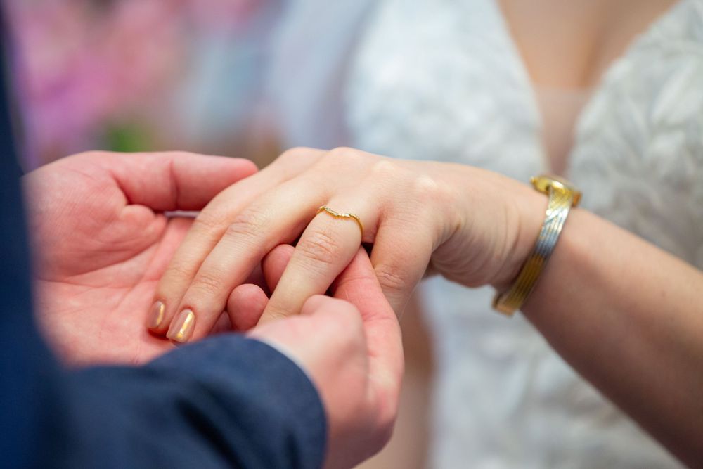 Close-up of wedding ring exchange, bride wearing gold bracelet receiving ring with orange nail polish.