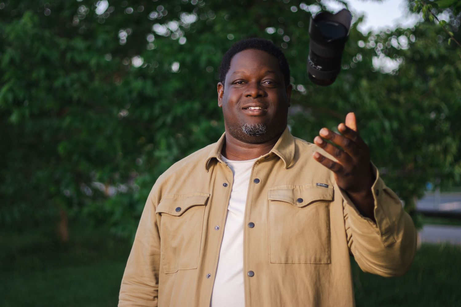 Someone in a tan jacket gestures while standing outdoors in a garden setting.