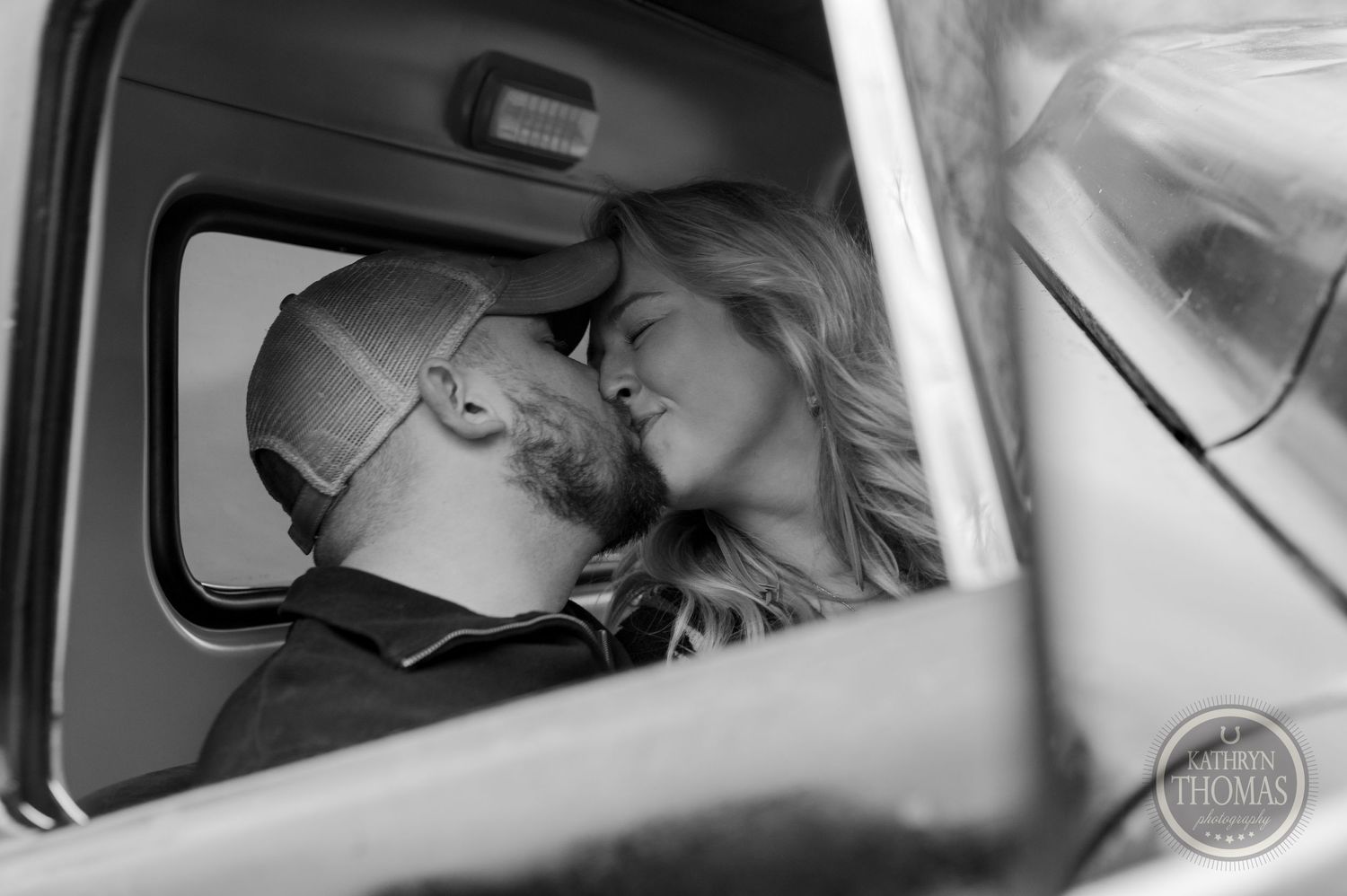 A black and white photo capturing a romantic moment inside a vintage truck cabin.