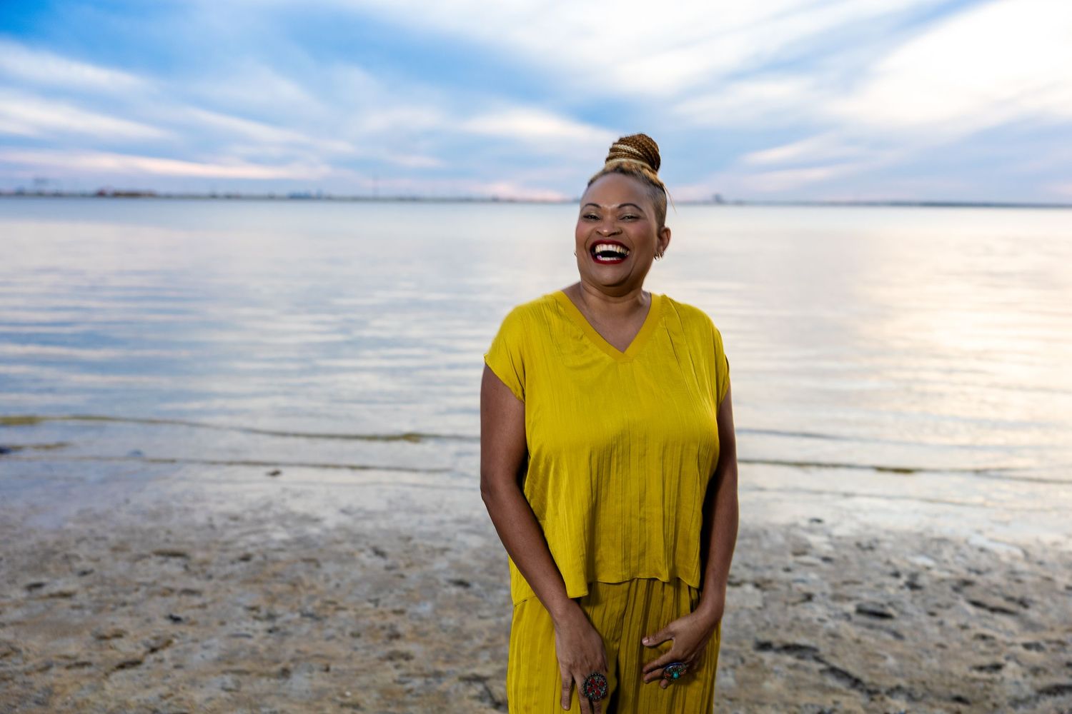 Person in yellow dress standing on beach at sunset with serene ocean view.