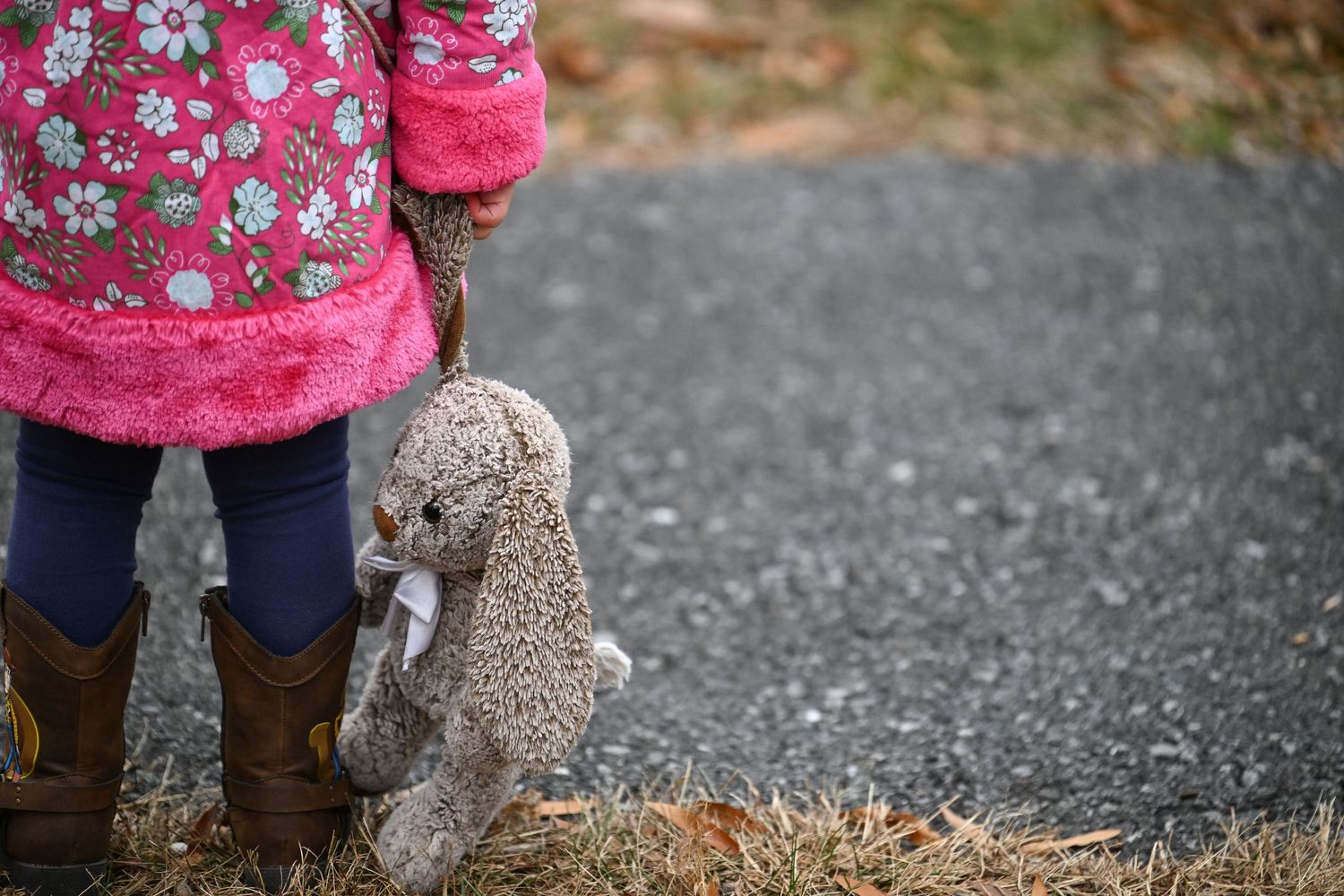 A photo of the bottom half of Emma standing, focusing on the stuffed bunny she holds at her side by the ear and her Toy Story cowgirl boots