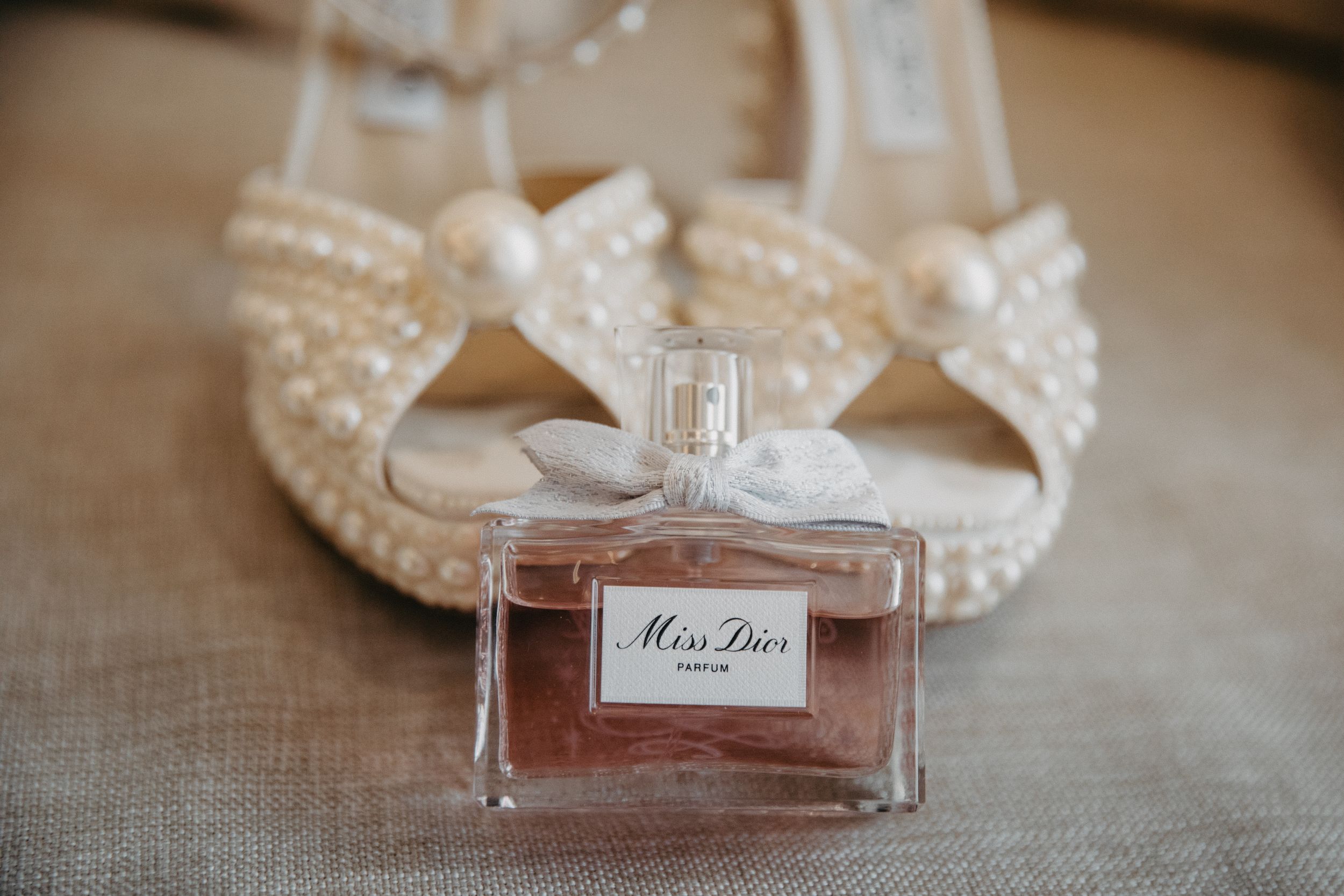 Miss Dior perfume bottle displayed with elegant beaded wedding shoes.