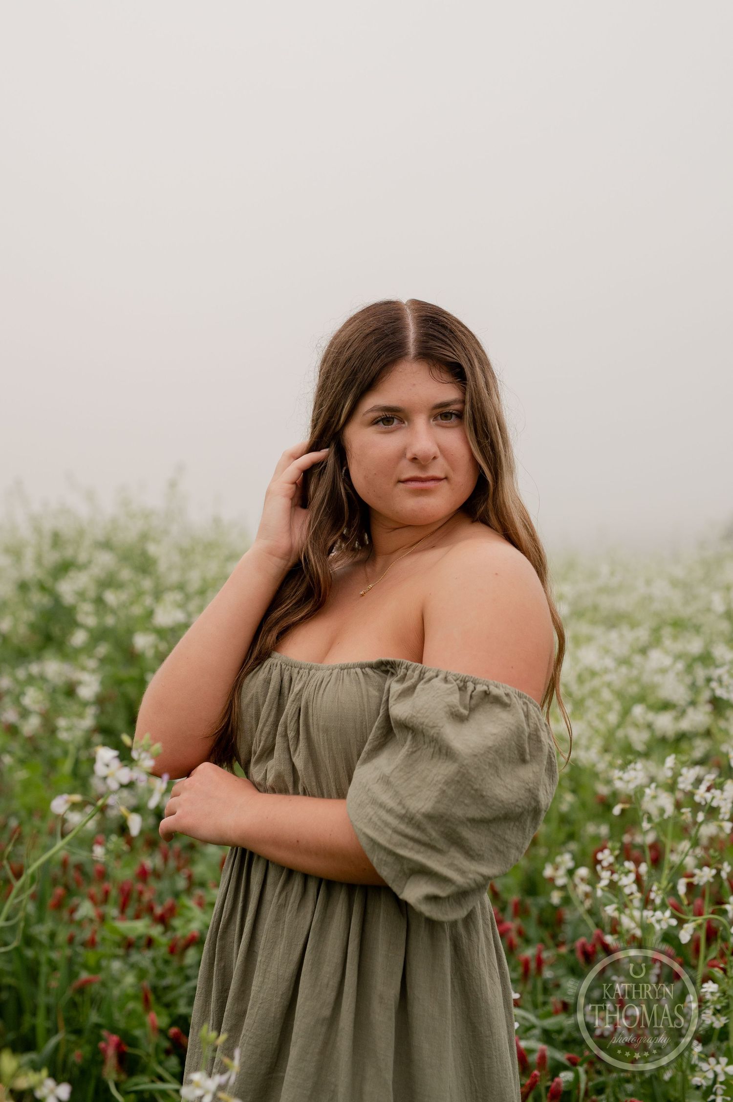 Person in green off-shoulder dress poses gracefully in a field of blooming white and red flowers.