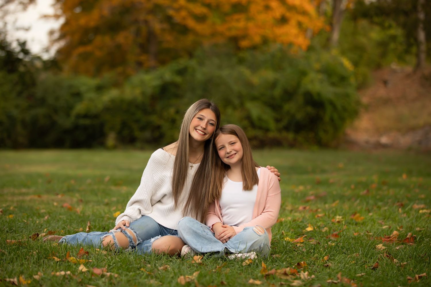 Two people lay on autumn grass surrounded by fallen leaves during a golden hour photoshoot.