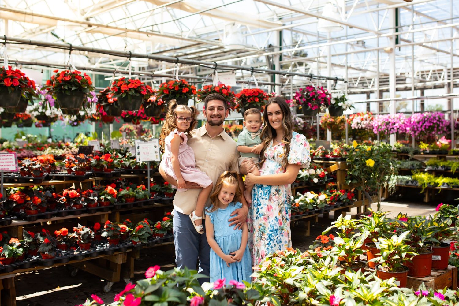 Shoppers browse colorful flowers and plants in a spacious greenhouse garden center filled with spring blooms and greenery.