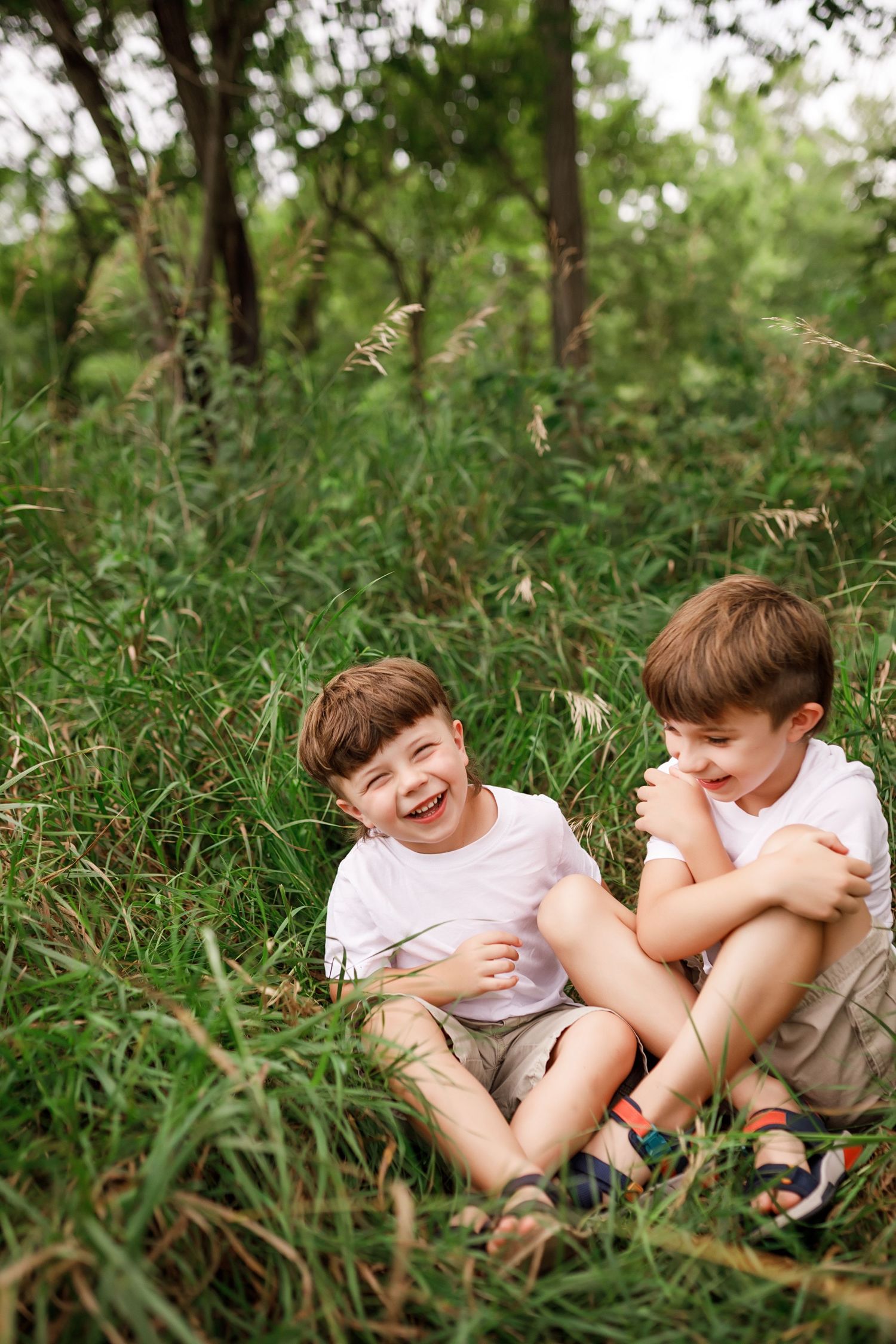 Two children lying in tall grass giggling and playing together on a summer day.