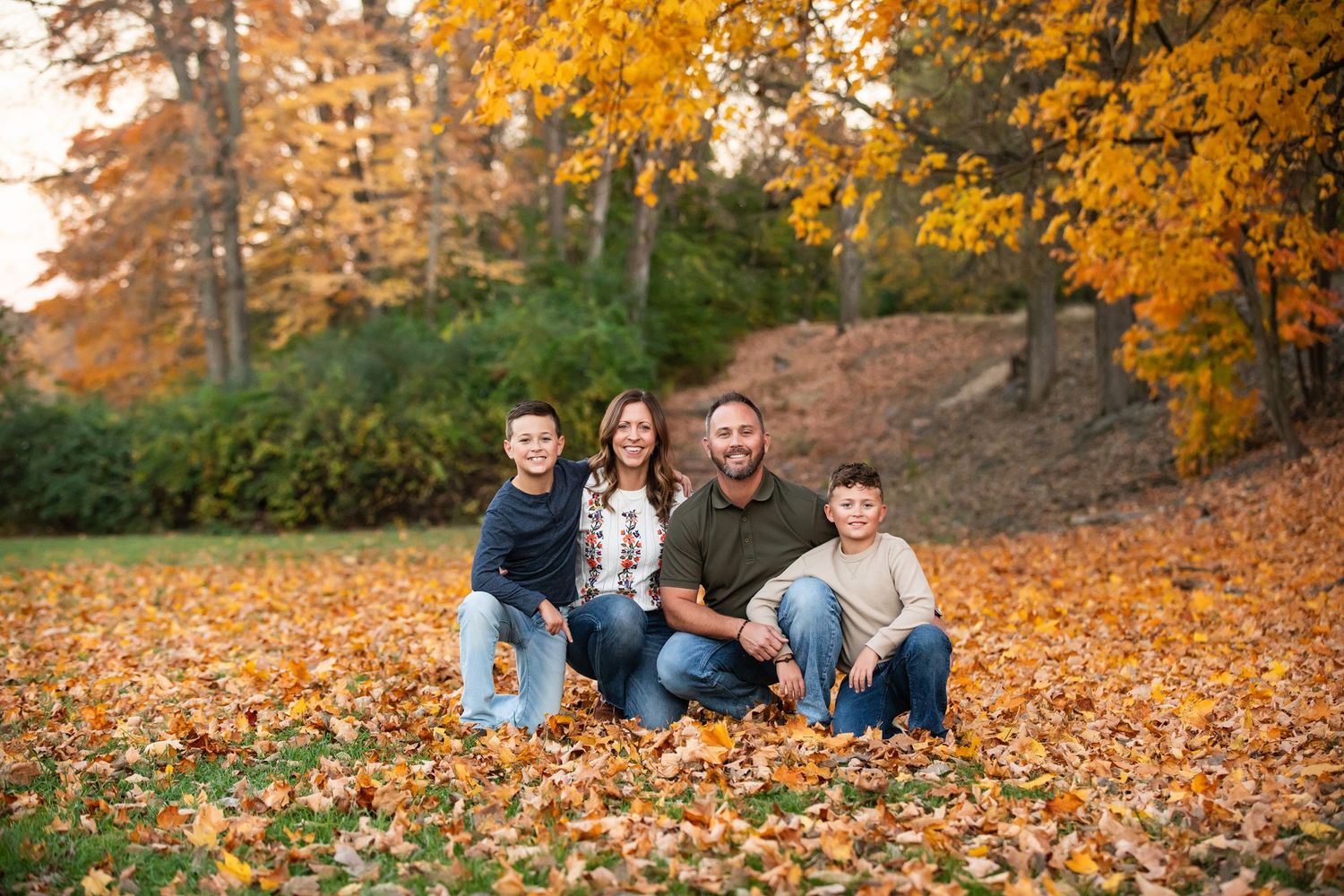 A group sits together in vibrant autumn leaves as golden fall foliage creates a warm seasonal backdrop.