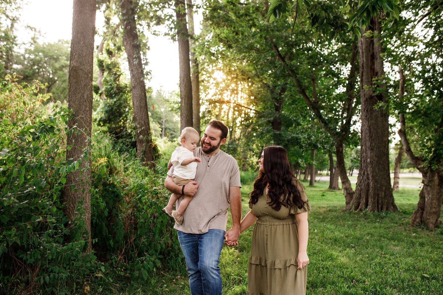 Family walking together through a sunlit wooded park on a warm summer evening.