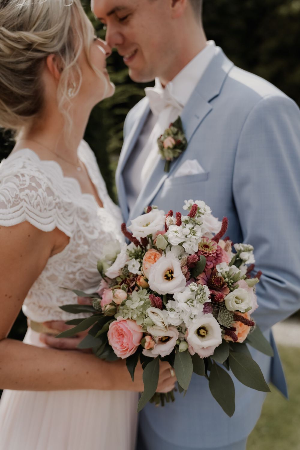 A couple shares an intimate moment while holding a lush bouquet of pink and white flowers.
