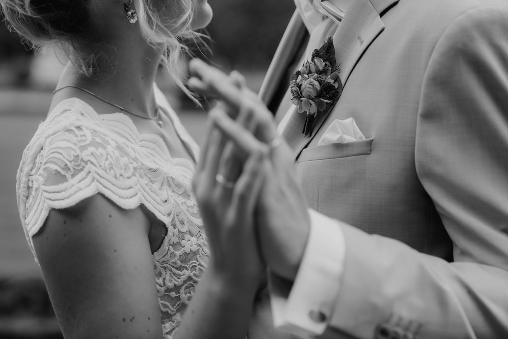 A romantic black and white closeup moment during a wedding ceremony with lace dress and boutonniere details.