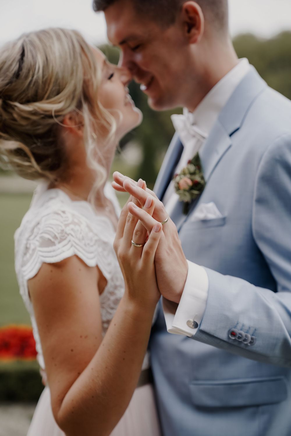 Intimate wedding portrait showing clasped hands and a light blue suit against an outdoor setting.